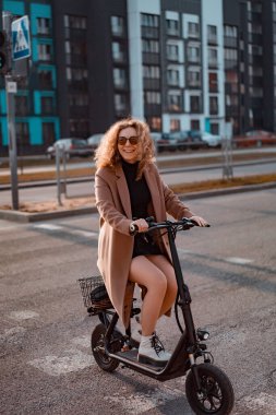 Genç ve güzel bir kadın işe elektrikli scooterla gidiyor, modern.