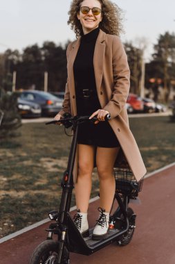 Genç ve güzel bir kadın işe elektrikli scooterla gidiyor, modern.