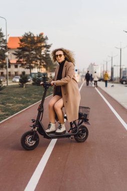 Genç ve güzel bir kadın işe elektrikli scooterla gidiyor, modern.