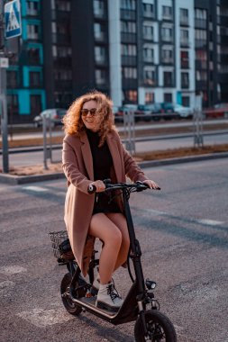 Genç ve güzel bir kadın işe elektrikli scooterla gidiyor, modern.