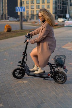 Genç ve güzel bir kadın işe elektrikli scooterla gidiyor, modern.