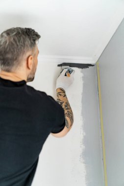 Onarım. Adam duvarları silindirle boyuyor, resim yapmaya hazırlanıyor, odada tamirat yapıyor. Duvarı boyayın..