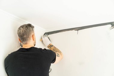 Onarım. Adam duvarları silindirle boyuyor, resim yapmaya hazırlanıyor, odada tamirat yapıyor. Duvarı boyayın..