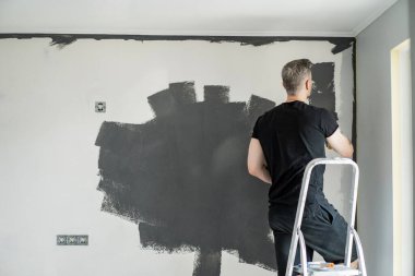 Onarım. Adam duvarları silindirle boyuyor, resim yapmaya hazırlanıyor, odada tamirat yapıyor. Duvarı boyayın..