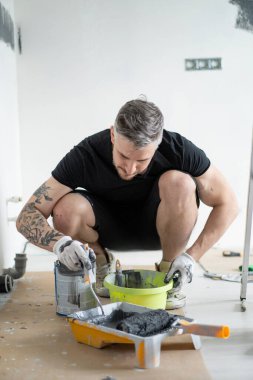 Onarım. Adam duvarları silindirle boyuyor, resim yapmaya hazırlanıyor, odada tamirat yapıyor. Duvarı boyayın..