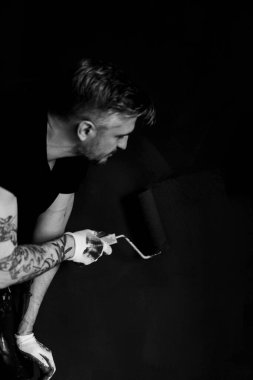 Onarım. Adam duvarları silindirle boyuyor, resim yapmaya hazırlanıyor, odada tamirat yapıyor. Duvarı boyayın..