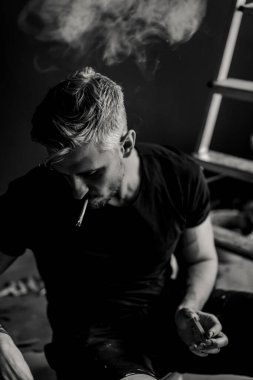 Orta yaşlı erkek portresi, genç çekici bir adam, yakın plan. Adam sigara içiyor, işe ara veriyor. siyah beyaz fotoğraf.