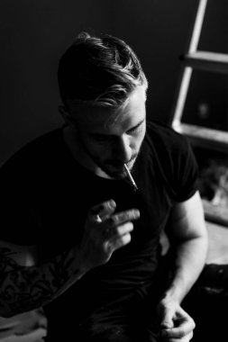 Orta yaşlı erkek portresi, genç çekici bir adam, yakın plan. Adam sigara içiyor, işe ara veriyor. siyah beyaz fotoğraf.