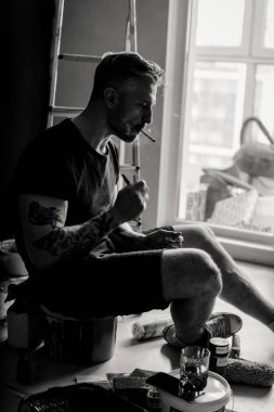 Orta yaşlı erkek portresi, genç çekici bir adam, yakın plan. Adam sigara içiyor, işe ara veriyor. siyah beyaz fotoğraf.