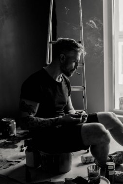 Orta yaşlı erkek portresi, genç çekici bir adam, yakın plan. Adam sigara içiyor, işe ara veriyor. siyah beyaz fotoğraf.