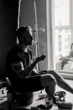 Orta yaşlı erkek portresi, genç çekici bir adam, yakın plan. Adam sigara içiyor, işe ara veriyor. siyah beyaz fotoğraf.