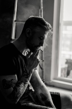 Orta yaşlı erkek portresi, genç çekici bir adam, yakın plan. Adam sigara içiyor, işe ara veriyor. siyah beyaz fotoğraf.