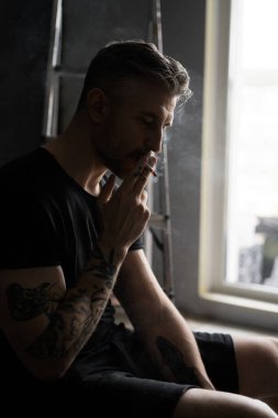 Orta yaşlı erkek portresi, genç çekici bir adam, yakın plan. Adam sigara içiyor, işe ara veriyor. siyah beyaz fotoğraf.