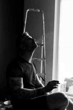 Orta yaşlı erkek portresi, genç çekici bir adam, yakın plan. Adam sigara içiyor, işe ara veriyor. siyah beyaz fotoğraf.