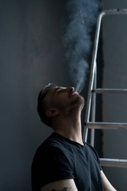 Orta yaşlı erkek portresi, genç çekici bir adam, yakın plan. Adam sigara içiyor, işe ara veriyor. siyah beyaz fotoğraf.