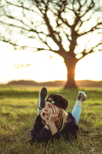 女性は夏の夕日を眺めながら芝生の上に横たわっています 夏の気分幸せ笑い — ストック写真