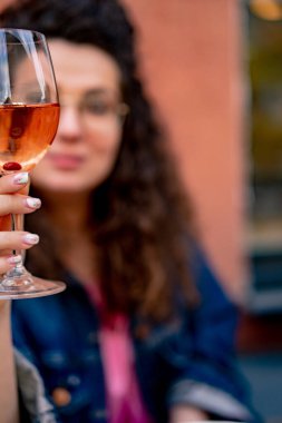 Bir sokak kafesinde bir bardak gül şarabıyla kıvırcık saçlı güzel bir genç kadın.