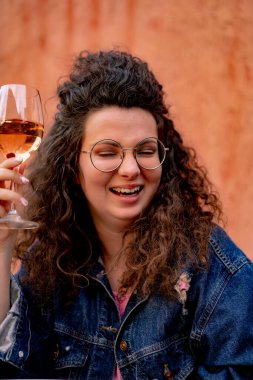 Bir sokak kafesinde bir bardak gül şarabıyla kıvırcık saçlı güzel bir genç kadın.