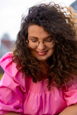 Pembe uzun elbiseli, gözlüklü, güzel, kahverengi kıvırcık saçlı kadın. Portre, yakın plan, hipster.