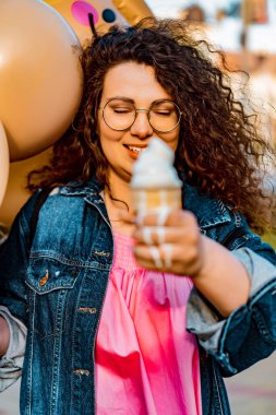 Pembe uzun elbiseli, sarı, altın ve siyah balonlu ve vanilyalı dondurma külahlı güzel, kahverengi kıvırcık saçlı kadın doğum günü partisine gitmek için caddede yürüyor.