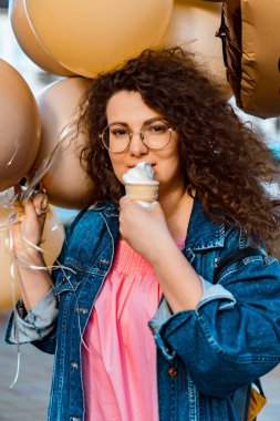 Pembe uzun elbiseli, sarı, altın ve siyah balonlu ve vanilyalı dondurma külahlı güzel, kahverengi kıvırcık saçlı kadın doğum günü partisine gitmek için caddede yürüyor.