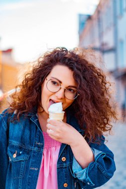 Pembe uzun elbiseli, sarı, altın ve siyah balonlu ve vanilyalı dondurma külahlı güzel, kahverengi kıvırcık saçlı kadın doğum günü partisine gitmek için caddede yürüyor.