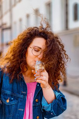 Pembe uzun elbiseli, sarı, altın ve siyah balonlu ve vanilyalı dondurma külahlı güzel, kahverengi kıvırcık saçlı kadın doğum günü partisine gitmek için caddede yürüyor.