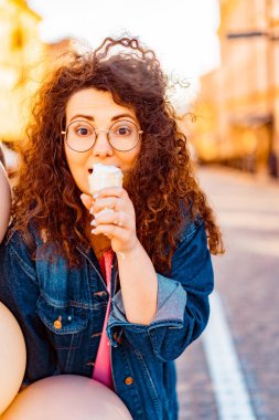 Pembe uzun elbiseli, sarı, altın ve siyah balonlu ve vanilyalı dondurma külahlı güzel, kahverengi kıvırcık saçlı kadın doğum günü partisine gitmek için caddede yürüyor.