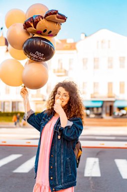 Pembe uzun elbiseli, sarı, altın ve siyah balonlu ve vanilyalı dondurma külahlı güzel, kahverengi kıvırcık saçlı kadın doğum günü partisine gitmek için caddede yürüyor.
