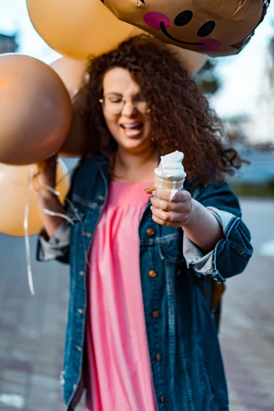 Pembe uzun elbiseli, sarı, altın ve siyah balonlu ve vanilyalı dondurma külahlı güzel, kahverengi kıvırcık saçlı kadın doğum günü partisine gitmek için caddede yürüyor.