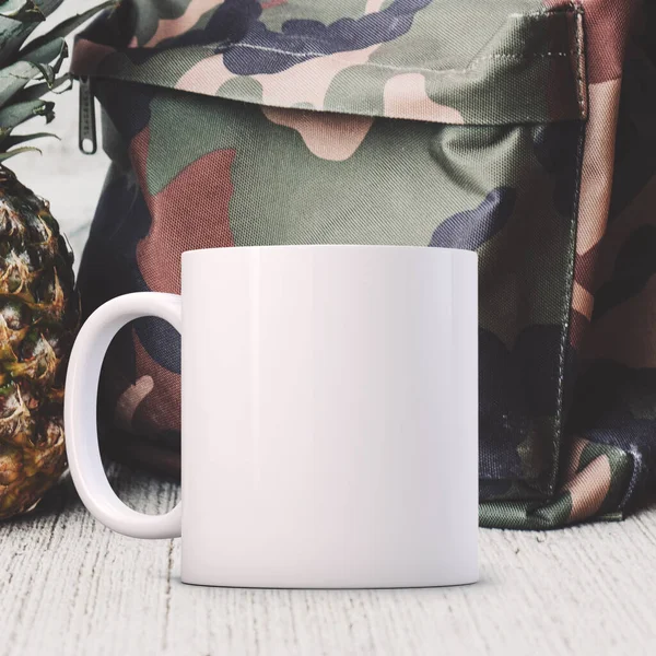 白色的Mug Mockup 在一个陆军织物背包前 很适合卖杯子的生意 只要把你的报价或设计贴在图片上就行了 — 图库照片