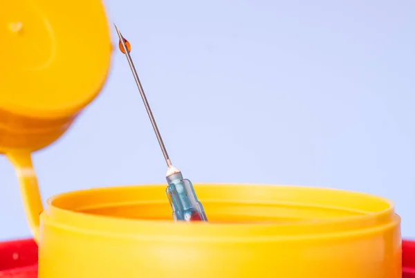Yellow medical disposal waste box, syringe needle with red drop on the tip — Stock Photo, Image
