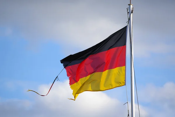 Bandera deshilachada de Alemania ondeando en el viento contra un cielo azul — Foto de Stock