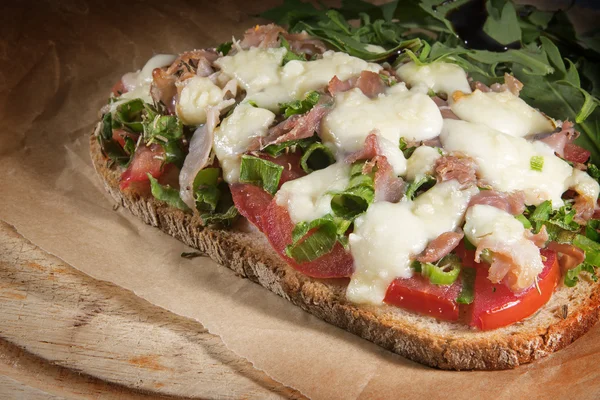 Gratiniertes Brot mit Tomaten, Frühlingszwiebeln, Speck und Mozzarella auf rustikalem Holz — Stockfoto