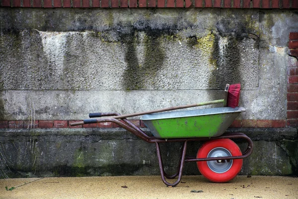 绿色的手推车与一个红色的车轮和红色的扫帚对一个古老的风化墙 — 图库照片