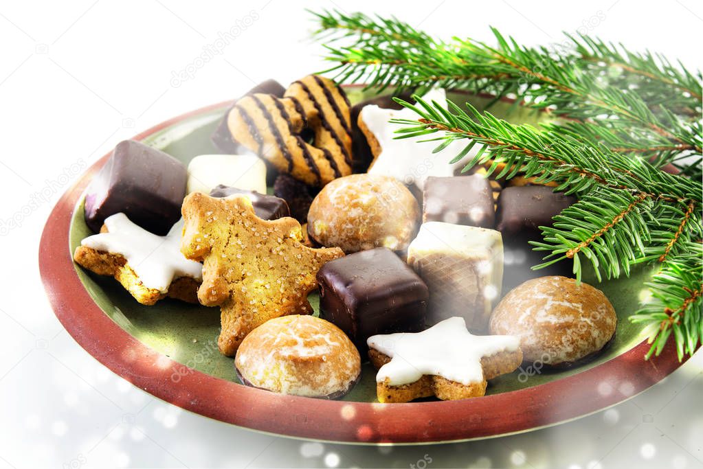 Christmas cookies, traditional gingerbread cakes, cinnamon stars and pepper nuts on a plate with fir branches and blurred snowy lights on a bright background