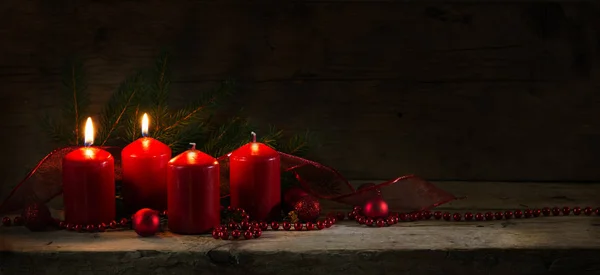 Quattro candele rosse, due delle quali accese al secondo avvento, decorazione natalizia su tavola rustica, fondo in legno scuro — Foto Stock