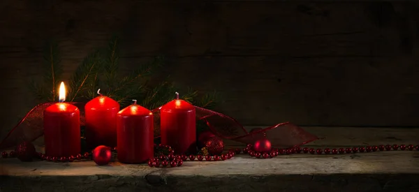 Four red candles, one of them burning on the first advent, christmas decoration on a rustic board, dark wooden background — Stock Photo, Image