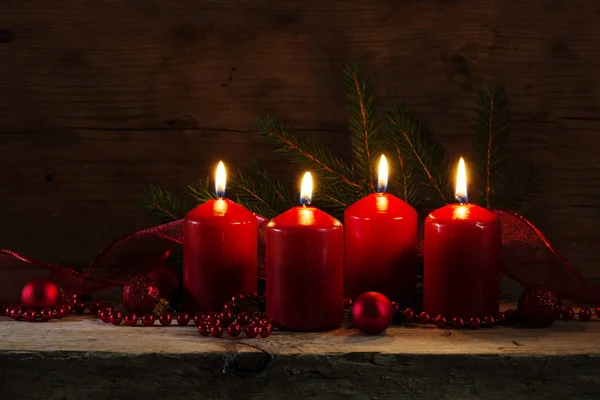 Quatro velas vermelhas acesas no quarto advento, decoração de Natal em uma placa rústica, fundo de madeira escuro — Fotografia de Stock