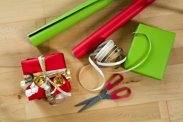 Csomagolás ajándékok piros és zöld papír, szalagok és olló, egy fából készült asztal karácsonyra, vagy Születésnap, felülnézet — Stock Fotó
