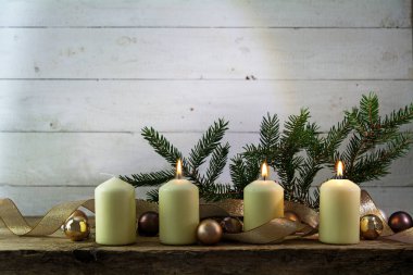 üç üçüncü advent, Noel dekorasyon Ladin twigs, baubles ile altın bir şerit bir rustik ahşap tahta karşı beyaz tahta üzerinde yanan mum beyaz