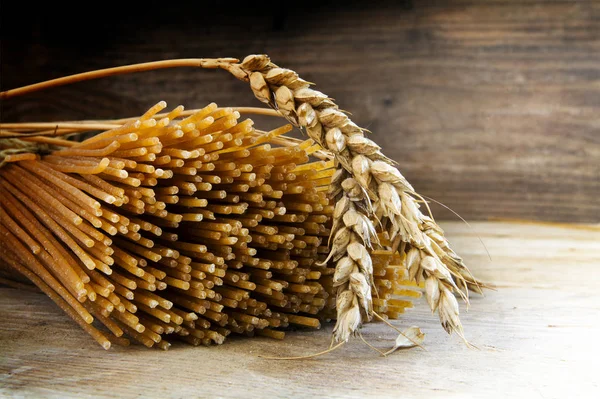 Biologische volkoren spaghetti en tarwe oren op een rustieke houten achtergrond — Stockfoto