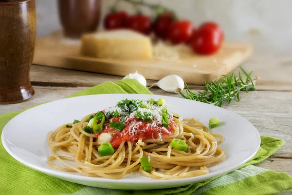 Macarrão de espaguete de trigo integral com molho de tomate fresco em uma mesa de madeira rústica, alguns ingredientes no fundo — Fotografia de Stock