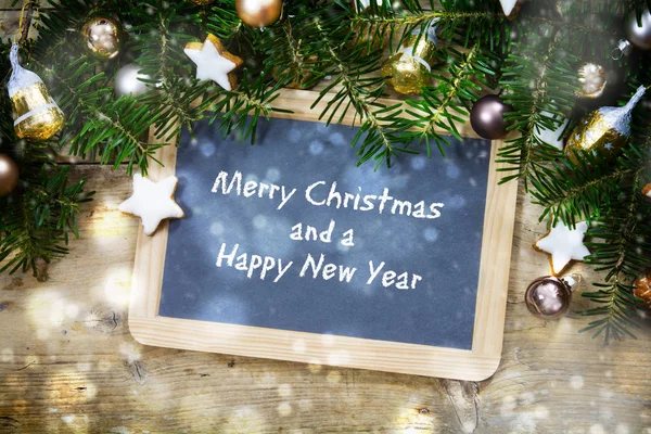 Slate writing board with fir tree branches, christmas balls and cookies on rustic wood, text Merry Christmas and a Happy New Year