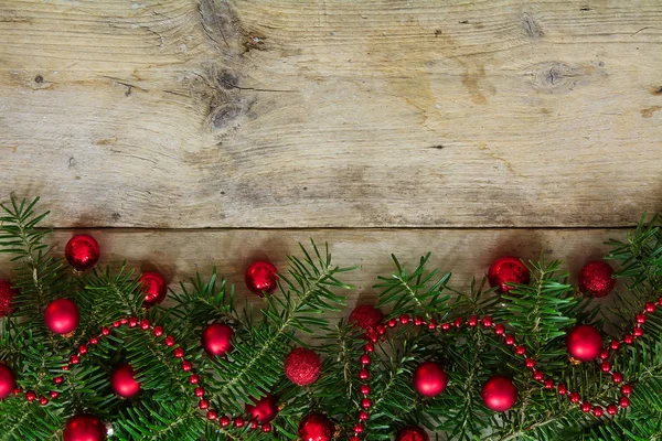 Spar boomtakken versierd met rode kerstballen als grens op een rustieke houten bord, vakantie achtergrond frame — Stockfoto