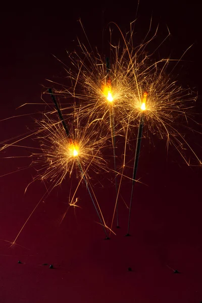 Three sparklers burning against a dark red background, party concept for new year, christmas or birthday, copy space — Stock Photo, Image