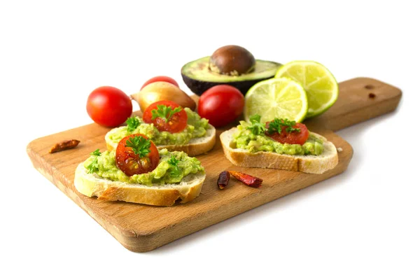 Канапе со сливками авокадо или гуакамоле с ингредиентами на кухонной доске, изолированные на белом фоне — стоковое фото
