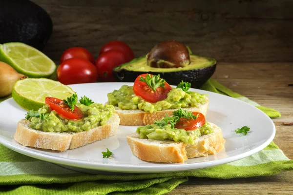 Crema de aguacate o guacamole en sándwiches de baguette con ingredientes en una mesa de cocina de madera rústica oscura —  Fotos de Stock