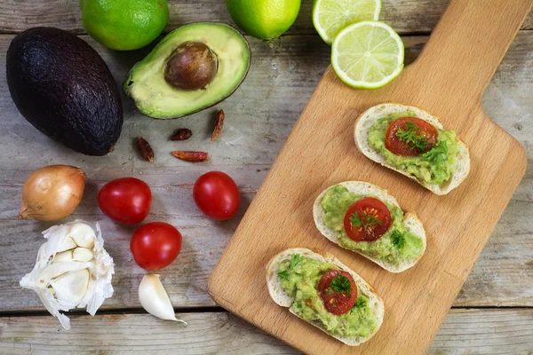 Crema di avocado o guacamole su tartine di baguette e ingredienti su una tavola di legno rustica, vista dall'alto — Foto Stock