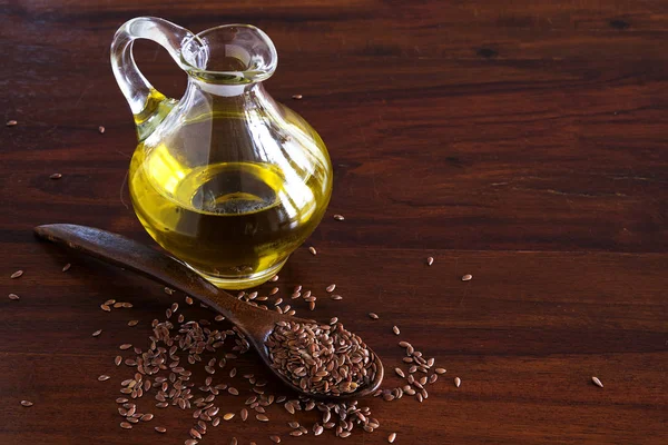 Leinsamen auf einem Löffel und Leinöl in einem Glaskrug auf einem dunklen Holztisch — Stockfoto